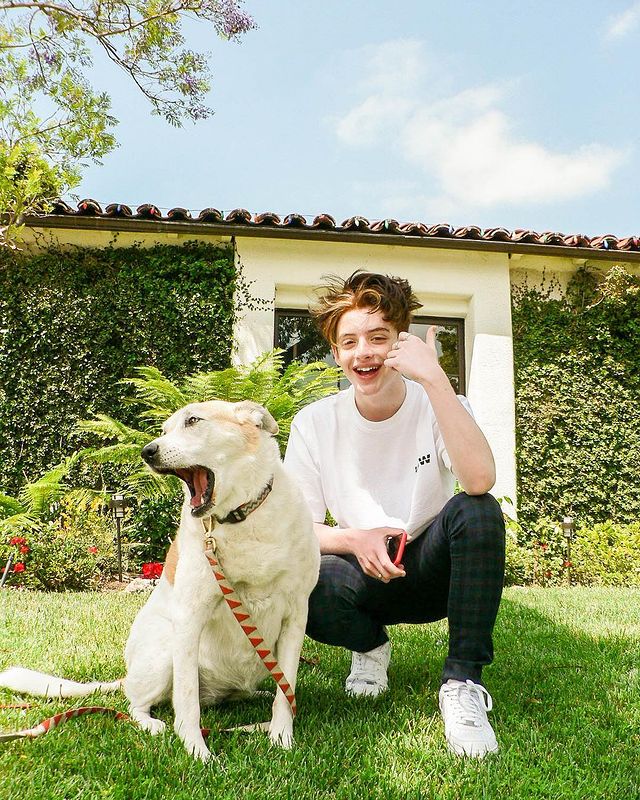 Thomas Barbusca in a white t-shirt and black pants posing with his dog pet.